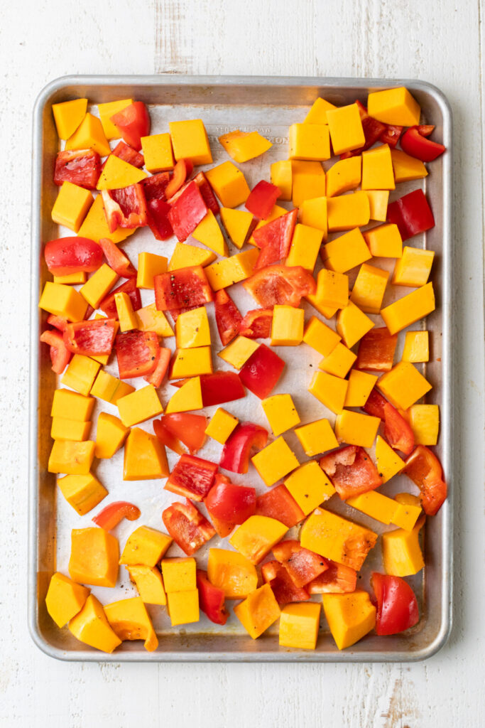 Cubed butternut quash and chopped red pepper on a sheet pan