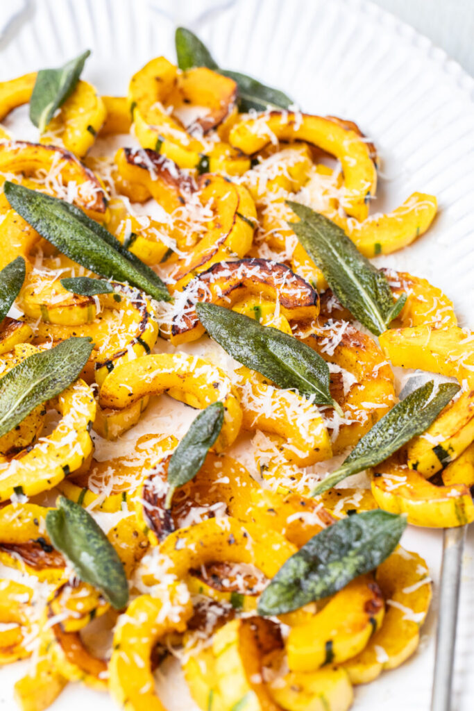 Delicata Squash on a serving platter with grated parmesan and crispy fried sage leaves