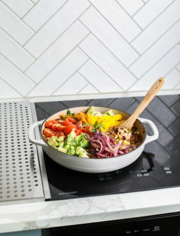 The ingredients for a one-pot Mexican quinoa bowl in a skillet on top of a Sharp 24 in. Induction Cooktop with Side Accessories (SCH2443GB).