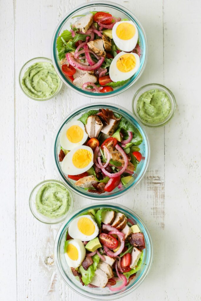 Three cobb salads in glass bowls with avocado green goddess dressing