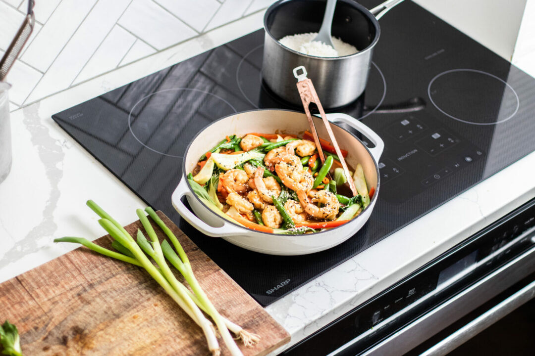 Shrimp and veggie stirfrying cooking in a pan on an induction cooktop