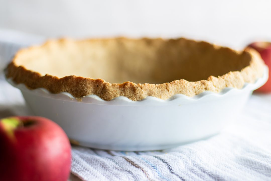 Pie crust in a bowl next to an apple.