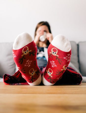 Woman sitting on a couch drinking out of a mug in holiday socks.