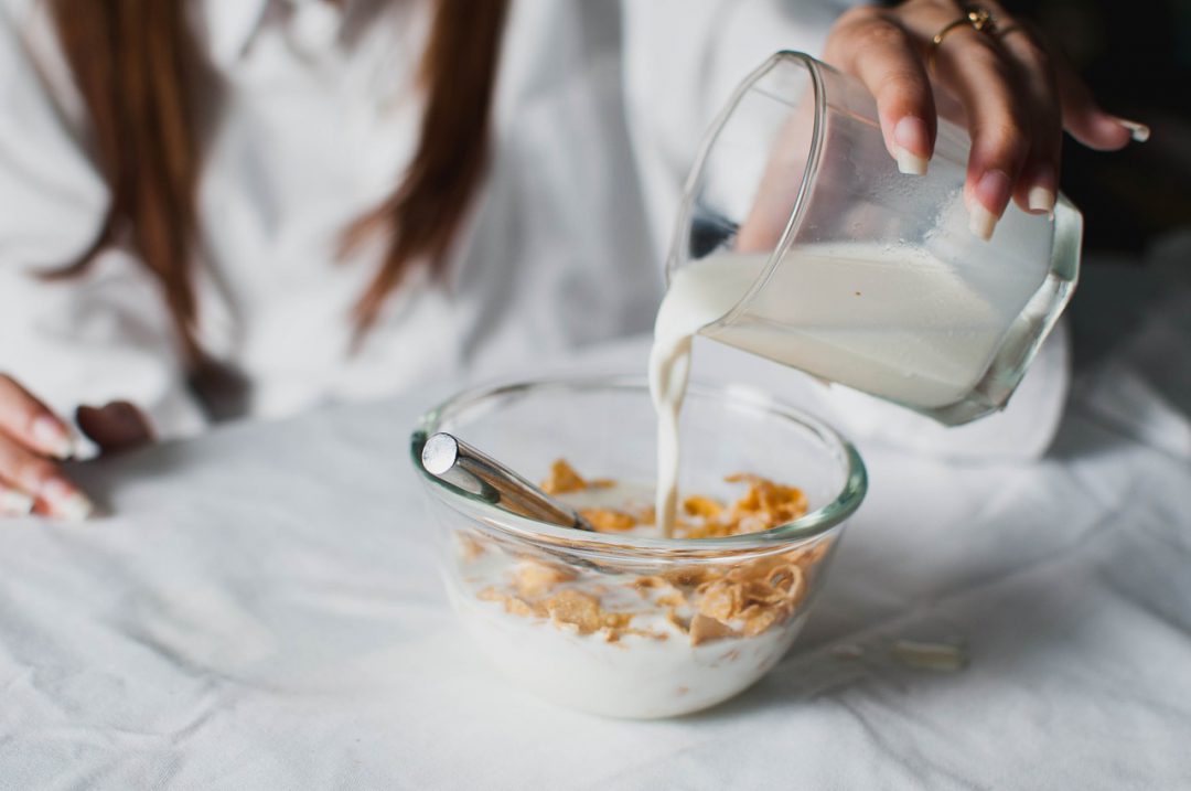 person pouring milk into bowl of cereal