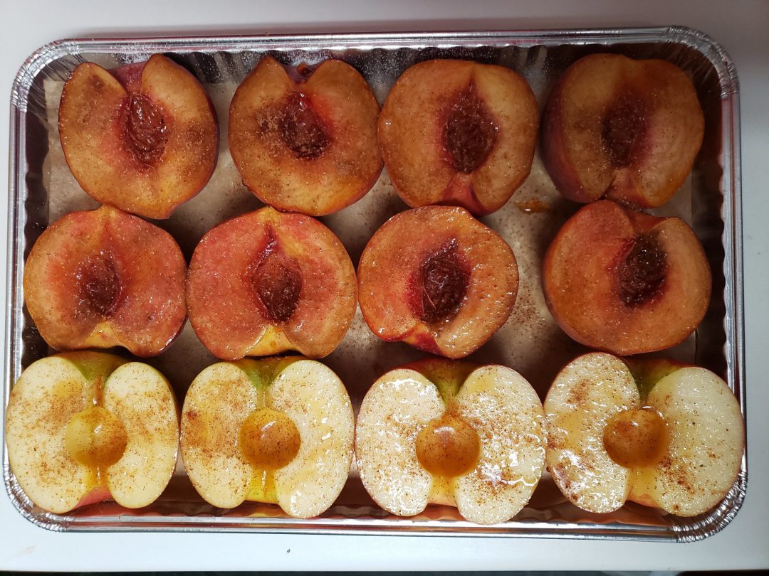Backed peaches and apples being prepared on a tray.