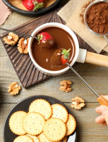 person dipping a strawberry in chocolate fondue