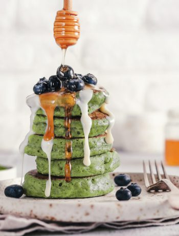 Matcha pancakes stacked on a plate with blueberries and syrup.