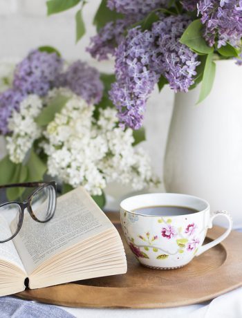 Floral arrangement next to a book and glasses.