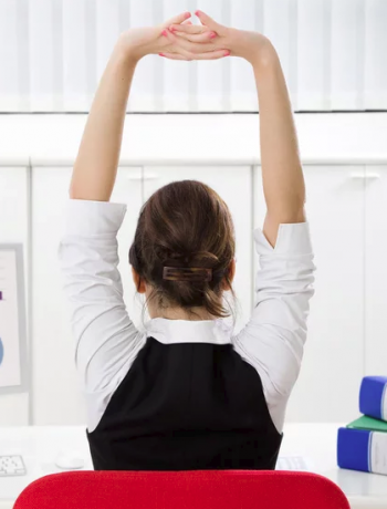 A woman sitting at her desk practicing different stretch techniques.