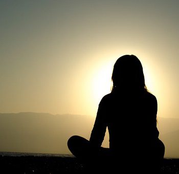 A woman meditating near a sunrise.