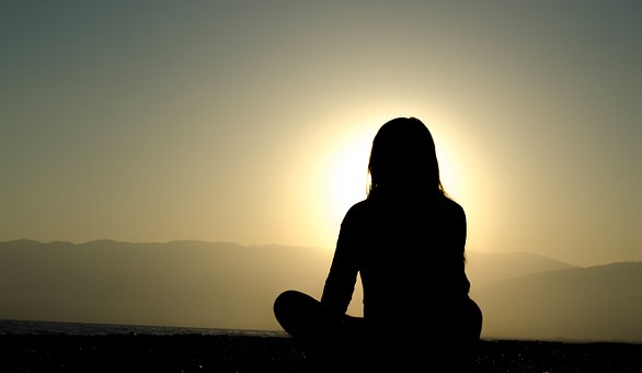 A woman meditating near a sunrise.