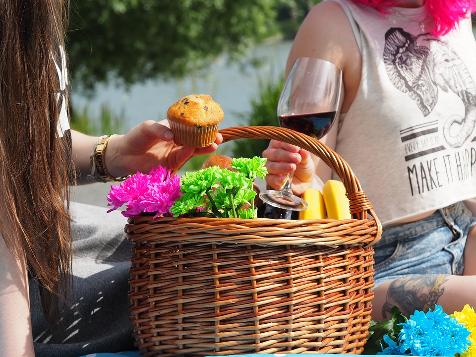 Picnic basket with flowers and foods including wine and muffins.