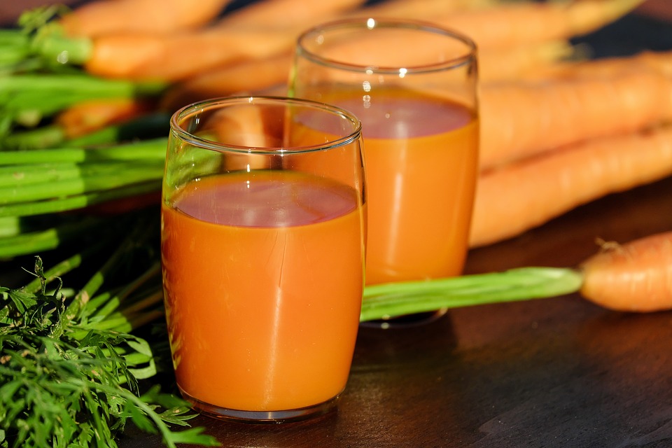 Carrot juice next to carrots on a wooden table.
