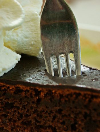 Fork pressing into chocolate cake with whipped cream.