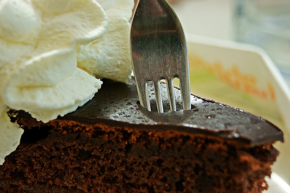 Fork pressing into chocolate cake with whipped cream.