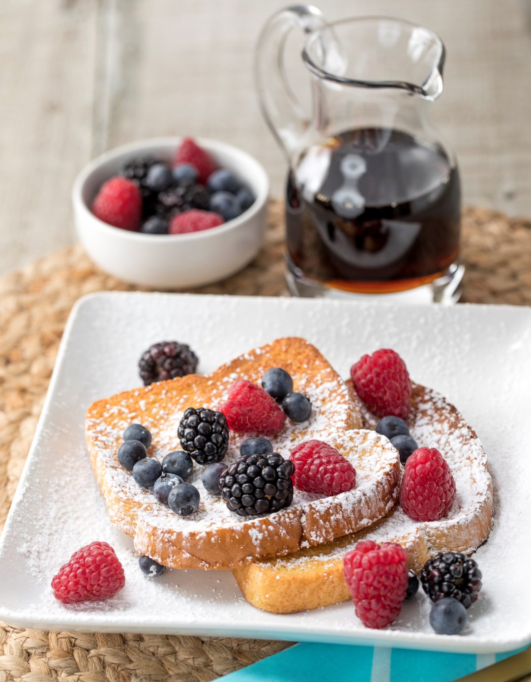 Toast on a plate with powder and rasberries next to syrup.