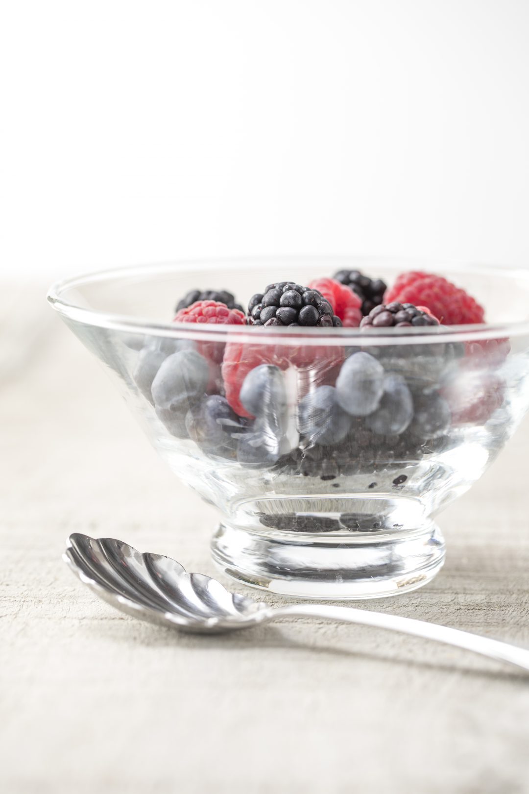 Rasberries and blueberries in a bowl next to a spoon.