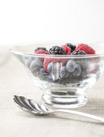 Rasberries and blueberries in a bowl next to a spoon.