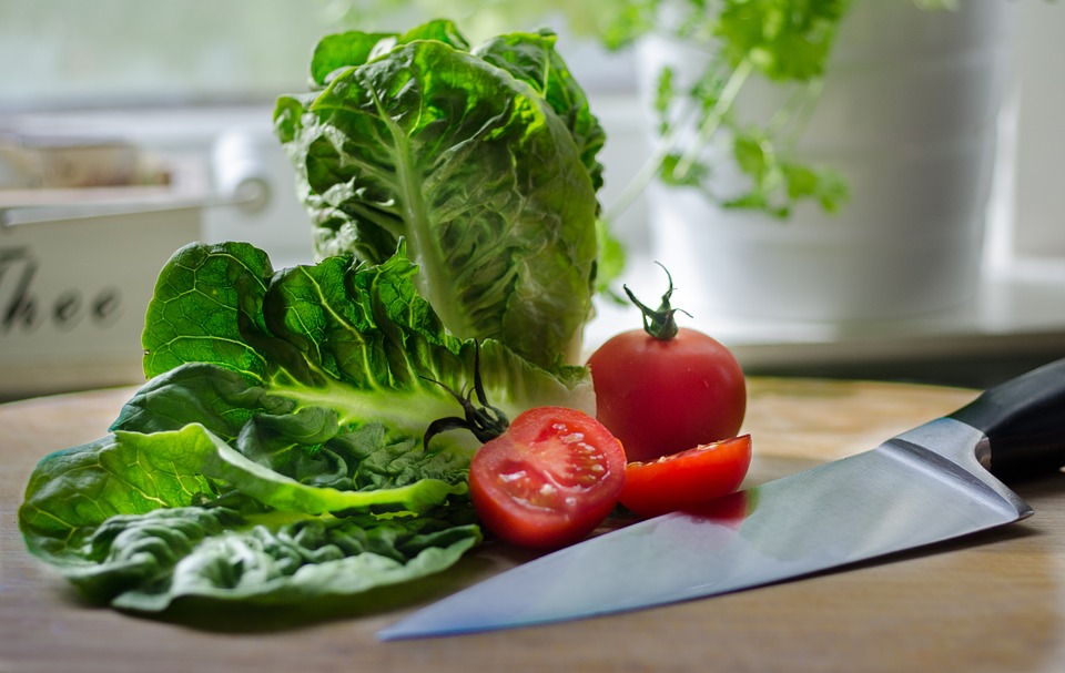 Lettuce and tomatoes on a cutting board next to a sharp knife in a kitchen.