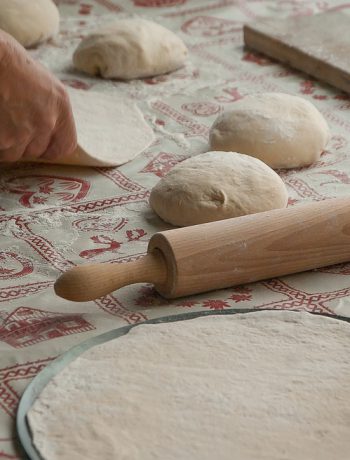 Pizza dough being rolled out on a table.