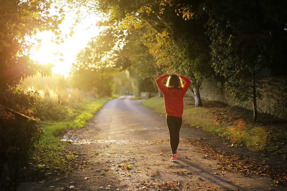 Woman exercising at dusk on a path near a wooded area.