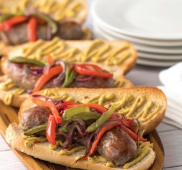 Grilled brats on a wooden surface with plates and napkins.
