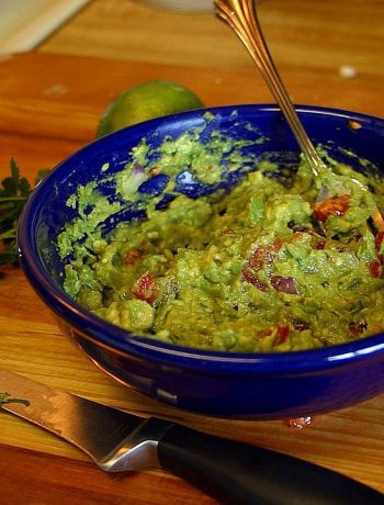 Blue bowl filled with guac and a spoon on a wooden surface.