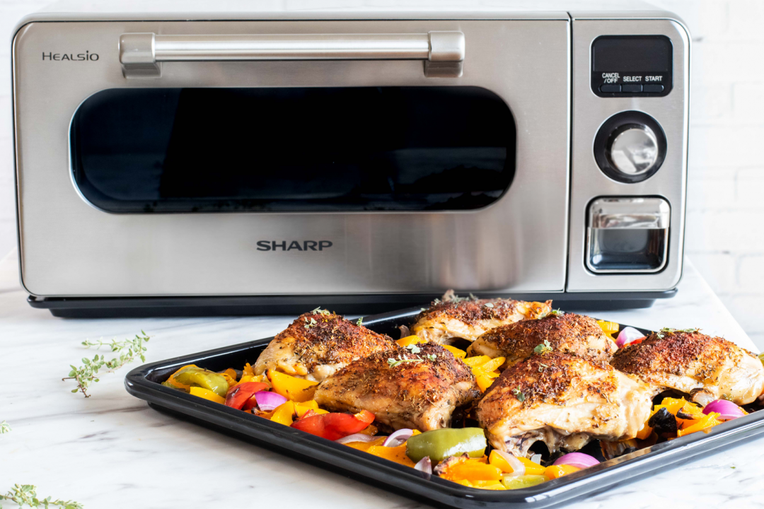 Meat dish with vegetables on a sheet pan in front of a Sharp Supersteam Countertop Oven.