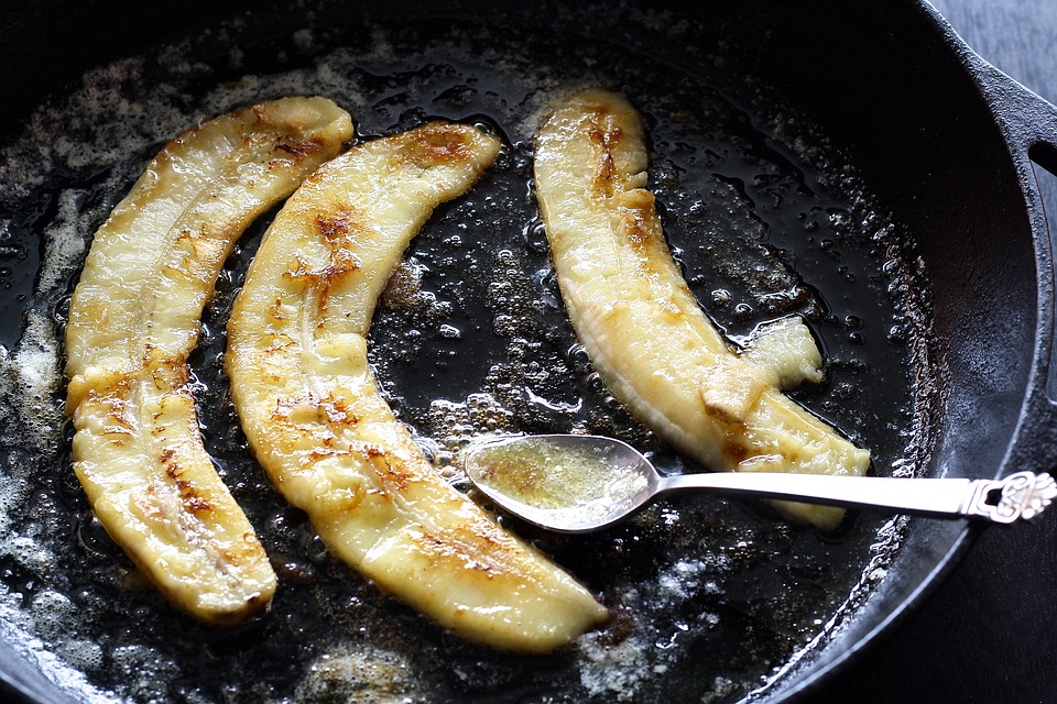 Bananas cooking in a pan next to a spoon.