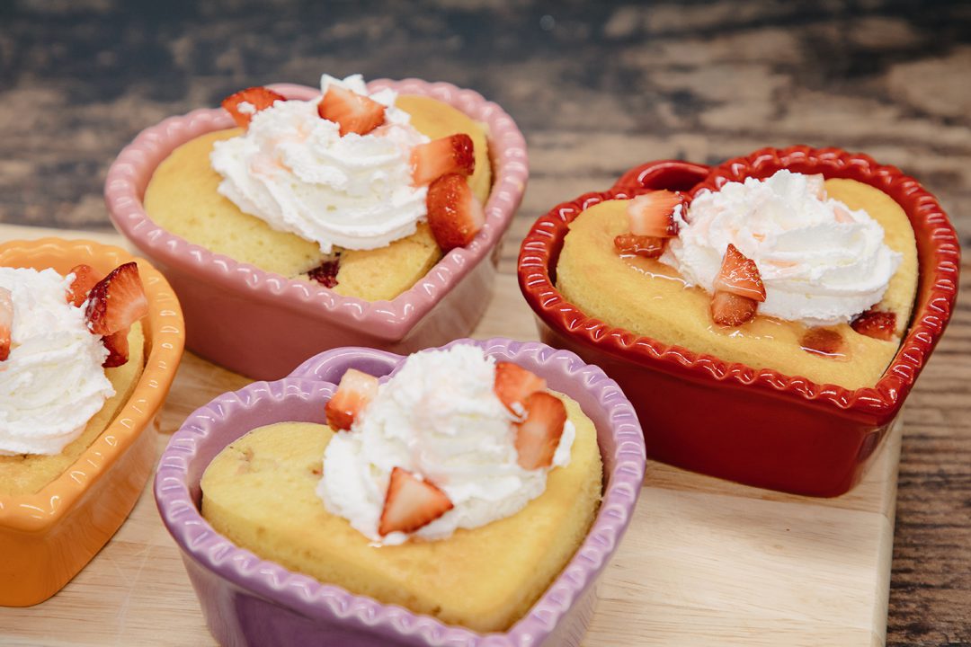 Four heart shaped strawberry shortcakes on a wooden surface.