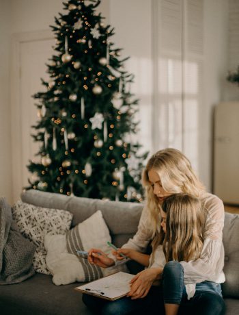 Mother and daughter sitting on a couch with a Christmas tree in the back.