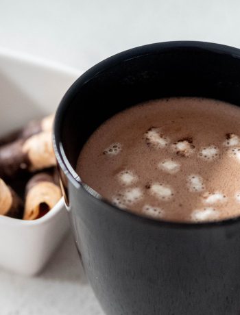 Hot chocolate with marshmellows next to a bowl of chocolate covered canolis.
