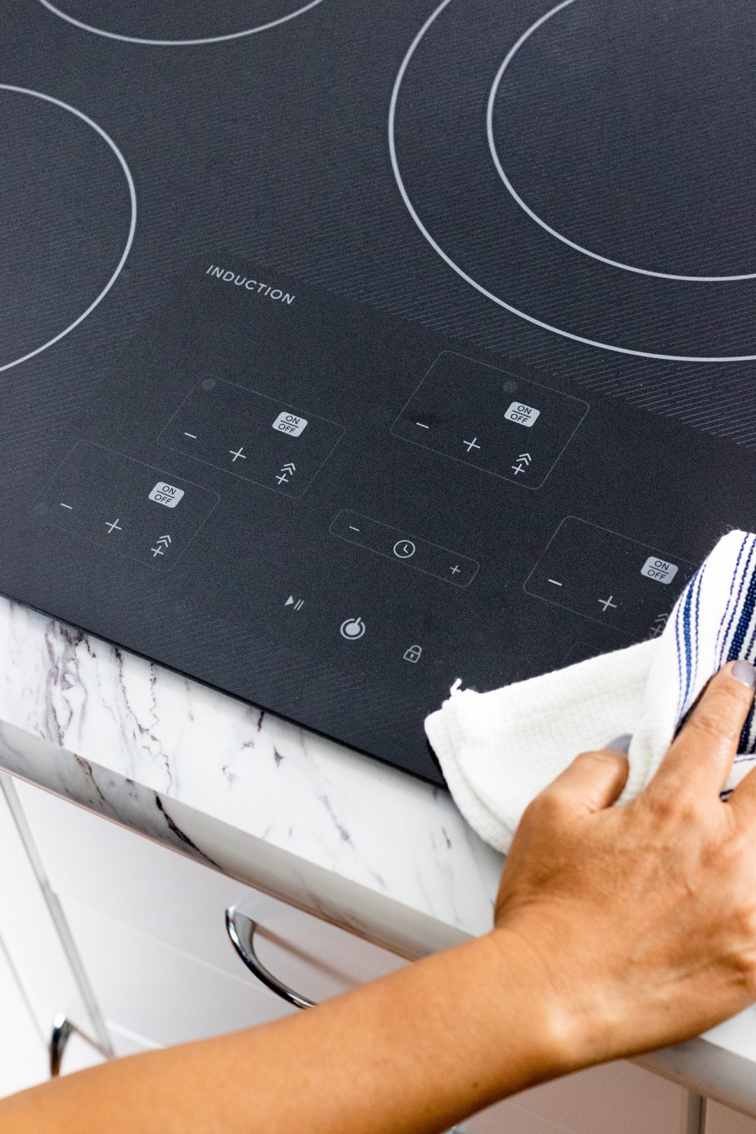 Someone cleaning an induction cooktop with a white rag.