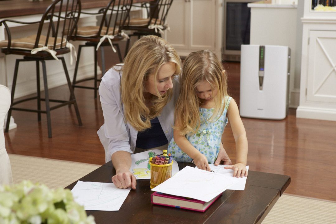 Mother and daughter coloring on a table near an air humidifier.