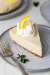 Lemon cheesecake slice on a plate with whipped cream and a piece of lemon on top