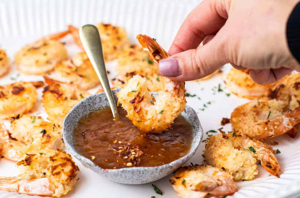 Baked coconut shrimp being dipped into sauce