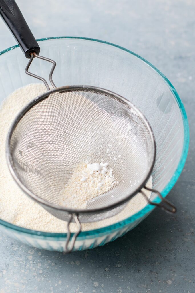 flour being sifted through a sifter into a bowl