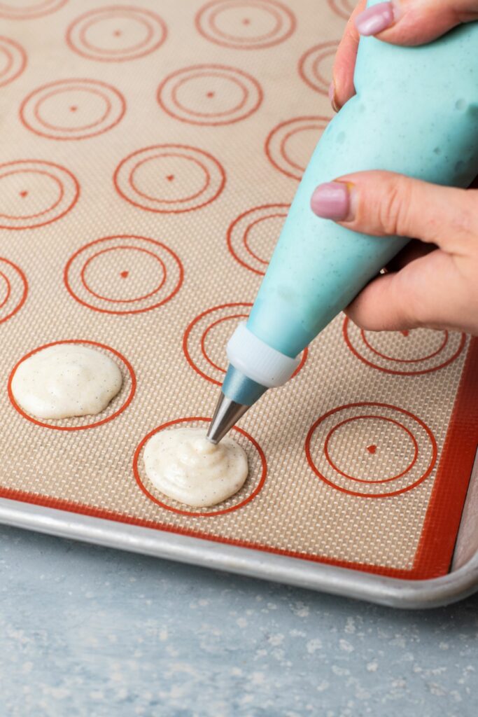 Vanilla bean macaron batter being piped onto a tray