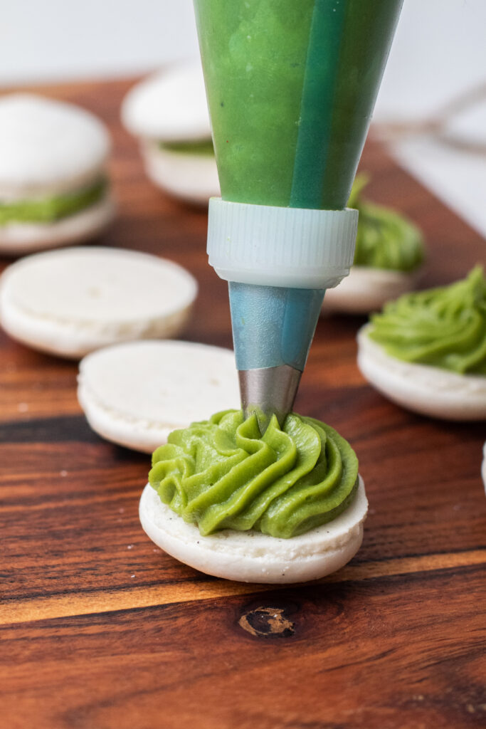 Matcha filling for macarons being piped onto vanilla bean macarons