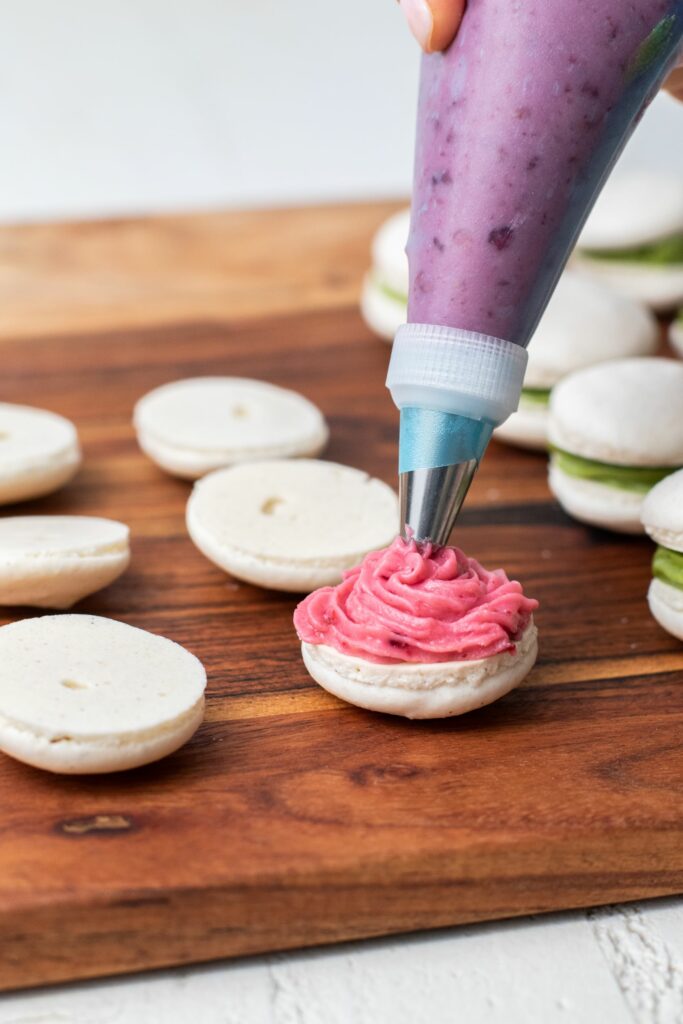 Baked macarons being piped with raspberry filling