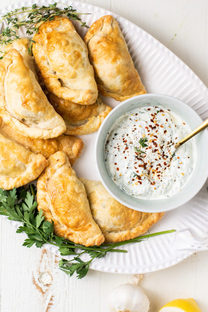 Empanadas with creamy chimichurri sauce on a serving platter