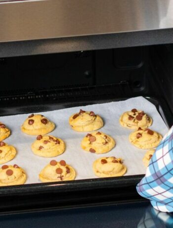 A user loading a tray of chocolate chip cookies into a Sharp Smart Combi Built-In Steam Oven.