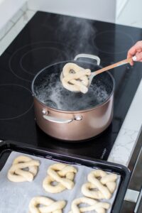 soft pretzels being dipped into water on cooktop