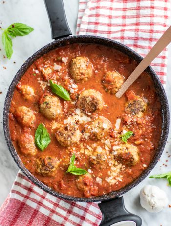Turkey meatballs in a pan with a wooden spoon on a red tablecloth.