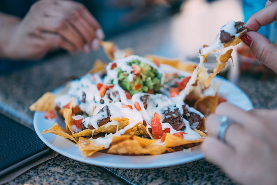 Nachos with toppings being spread apart and shared by three people.