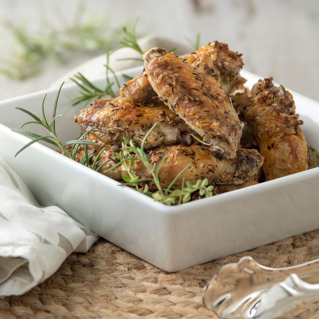 Chicken wings in a square dish on a wicker surface.