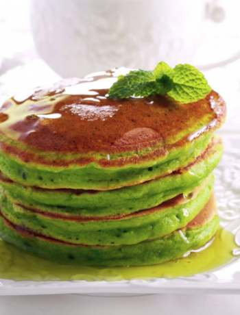 Matcha pancakes stacked upon one another on a white plate.