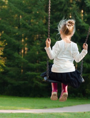 Young girl on a swing facing a wooded areas.