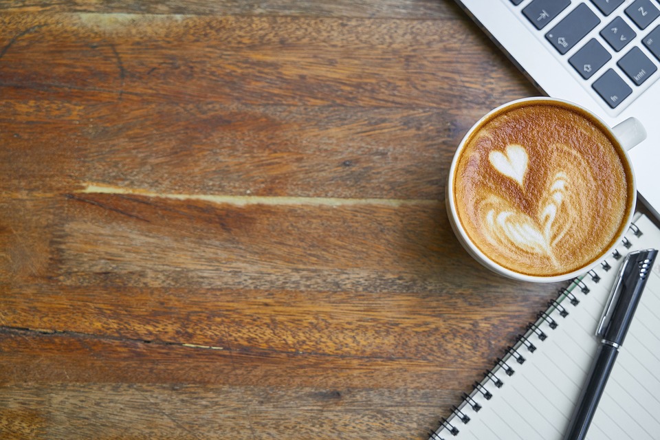 Coffee mug with a heart next to a workspace.
