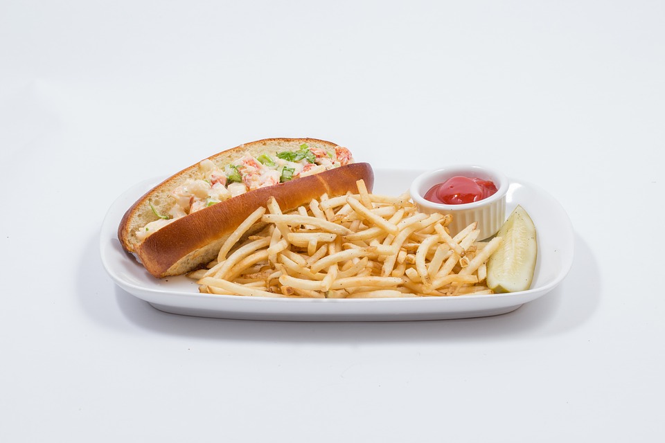 Lobster roll on a plate with french fries, ketchup, and a pickle.